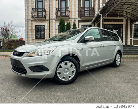Silver car parked outside a building on a cloudy day in a quiet area with few trees and a clear path 139842977