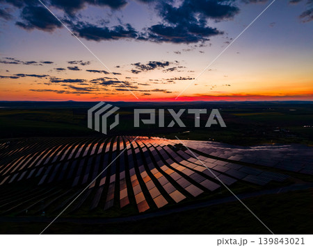 Sunset over solar panels reflecting light in the evening sky near a green landscape in a rural area during twilight hours Sunset over solar panels reflecting light in the evening sky near a green landscape in a rural area during twilight hours 139843021