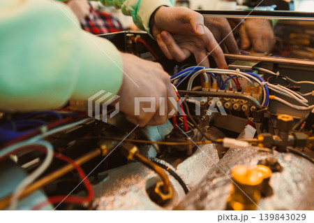 Technician repairs wires and components inside a vehicle engine at an auto shop during the day Technician repairs wires and components inside a vehicle engine at an auto shop during the day 139843029