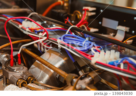 Close view of wires and connections in a mechanical device inside a workshop during repair work with tools and equipment present in the background Close view of wires and connections in a mechanical device inside a workshop during repair work with tools and equipment present in the background 139843030