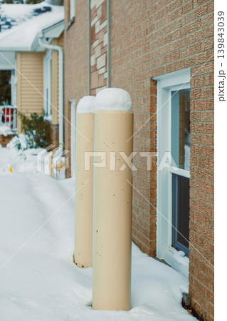 Snow covers two poles next to a building with a dusting of white in winter near the window and side of the structure in a neighborhood setting Snow covers two poles next to a building with a dusting of white in winter near the window and side of the structure in a neighborhood setting 139843039
