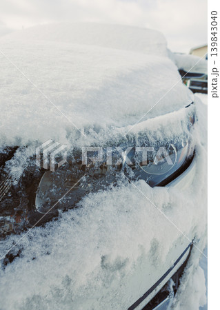 Snow covers a parked car in a residential area, showing only parts of the vehicle under a thick layer of white frost and ice during winter 139843040