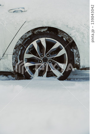 Winter scene shows a car wheel stuck in deep snow in a cold landscape during a snowfall Winter scene shows a car wheel stuck in deep snow in a cold landscape during a snowfall 139843042