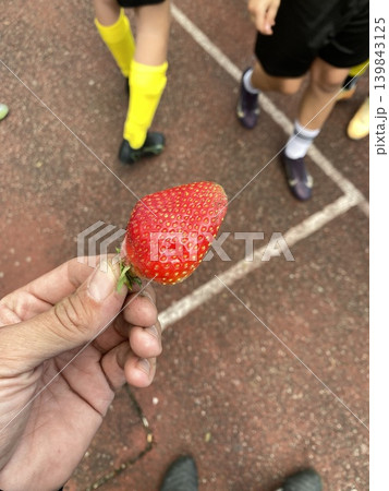 Child on playground offers heartshaped strawberry to someone nearby in candid summer moment Child on playground offers heartshaped strawberry to someone nearby in candid summer moment 139843125