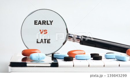 A magnifying glass highlights Early VS Late on a white surface, surrounded by various colored pills 139843299