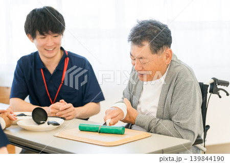 調理器具を使ってリハビリするシニア男性の補助をする作業療法士,ケアマネージャーのスタッフ 調理器具を使ってリハビリするシニア男性の補助をする作業療法士,ケアマネージャーのスタッフ 139844190