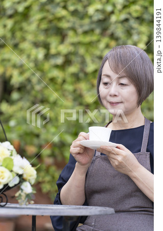 庭でガーデニングをしながらコーヒーを飲むシニア女性 庭でガーデニングをしながらコーヒーを飲むシニア女性 139844191