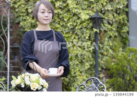 庭でガーデニングをしながらコーヒーを飲むシニア女性 庭でガーデニングをしながらコーヒーを飲むシニア女性 139844199