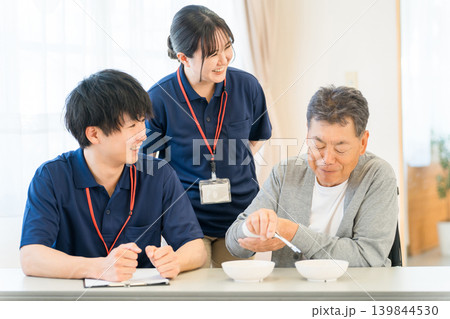 介護施設,病院,リハビリセンターで豆つかみトレーニンングをする男性患者と介護士の男女スタッフ 139844530
