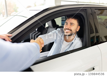 Young male customer shaking hands with professional salesman from inside new automobile 139844536