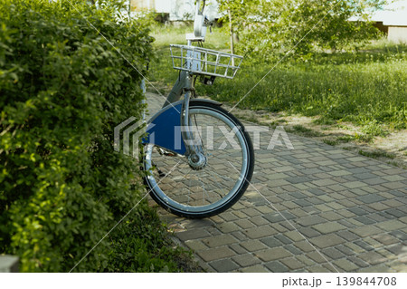 City bicycle parked near green bushes on sunny path. Eco friendly urban transport, sustainable lifestyle, everyday commuting and slow living concept. Natural light, authentic outdoor scene. Eco bike. City bicycle parked near green bushes on sunny path. Eco friendly urban transport, sustainable lifestyle, everyday commuting and slow living concept. Natural light, authentic outdoor scene. Eco bike. 139844708