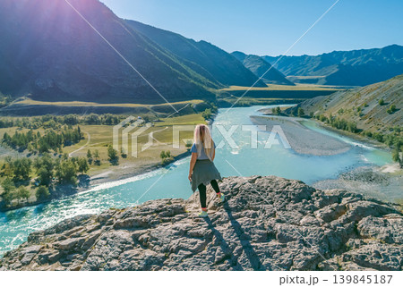 A lone traveler stands on a high rock overlooking the bright blue Katun River as it carves through the majestic Altai Mountains 139845187