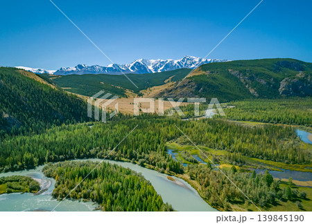 Beautiful summer panorama across Altai, showing a curving river winding through green valleys. Majestic snow-covered peaks stand tall in the horizon. Beautiful summer panorama across Altai, showing a curving river winding through green valleys. Majestic snow-covered peaks stand tall in the horizon. 139845190