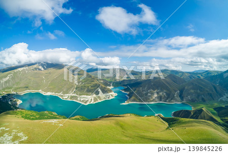Panoramic view capturing Lake Kazenoy's striking turquoise waters contrasting with steep, sun-kissed mountains under bright blue sky 139845226