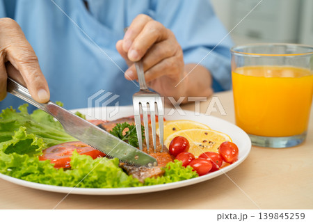 Asian elderly woman patient eating salmon stake and vegetable salad for healthy food in hospital. Asian elderly woman patient eating salmon stake and vegetable salad for healthy food in hospital. 139845259