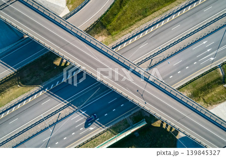 Aerial view of a multi-level highway interchange with a bridge crossing several roads. Car drives during the bright sunny day Aerial view of a multi-level highway interchange with a bridge crossing several roads. Car drives during the bright sunny day 139845327