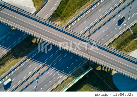 Aerial view of a multi-level highway interchange with a bridge crossing several roads. Cars drive during the bright sunny day Aerial view of a multi-level highway interchange with a bridge crossing several roads. Cars drive during the bright sunny day 139845328