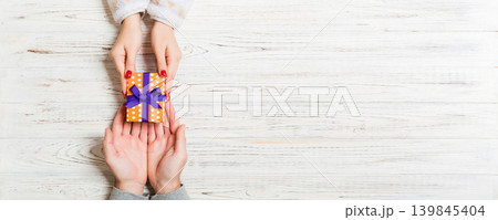 Top view of a gift in male and female hands on wooden background. Congratulation of each other concept. Copy space 139845404