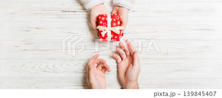Top view of holding a gift in female and male hands on wooden background. Woman and man give and receive a present. Close up of time for holiday concept Top view of holding a gift in female and male hands on wooden background. Woman and man give and receive a present. Close up of time for holiday concept 139845407