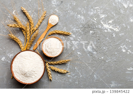 Flat lay of Wheat flour in wooden bowl with wheat spikelets on colored background. world wheat crisis Flat lay of Wheat flour in wooden bowl with wheat spikelets on colored background. world wheat crisis 139845422