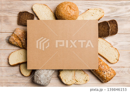 Minimalist paper blank mockup on background of Types of homemade bread. Different kinds of fresh bread as background, top view with space for your text or design Minimalist paper blank mockup on background of Types of homemade bread. Different kinds of fresh bread as background, top view with space for your text or design 139846153