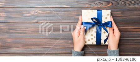 Top view of female hands holding christmas or other holiday handmade present box package in the palms, flat lay on dark table background with copy space Top view of female hands holding christmas or other holiday handmade present box package in the palms, flat lay on dark table background with copy space 139846180