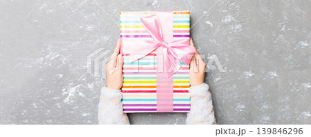 Woman arms holding gift box with colored ribbon on gray cement table background, top view and copy space for you design Woman arms holding gift box with colored ribbon on gray cement table background, top view and copy space for you design 139846296