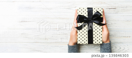 Top view of female hands holding christmas or other holiday handmade present box package in the palms, flat lay on white rustic table background with copy space 139846303