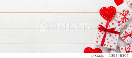 Valentine or other holiday handmade present in paper with red hearts and gifts box in holiday wrapper. Present box gift on wooden table top view with copy space, empty space for design Valentine or other holiday handmade present in paper with red hearts and gifts box in holiday wrapper. Present box gift on wooden table top view with copy space, empty space for design 139846305