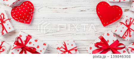 Valentine or other holiday handmade present in paper with red hearts and gifts box in holiday wrapper. Present box of gift on white wooden table top view with copy space, empty space for design Valentine or other holiday handmade present in paper with red hearts and gifts box in holiday wrapper. Present box of gift on white wooden table top view with copy space, empty space for design 139846308