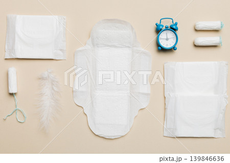 Ringing alarm clock with sanitary female tampons and menstrual sanitary pads. Medical concept of woman critical days and menstruation. Female daily hygiene. Copy space Ringing alarm clock with sanitary female tampons and menstrual sanitary pads. Medical concept of woman critical days and menstruation. Female daily hygiene. Copy space 139846636