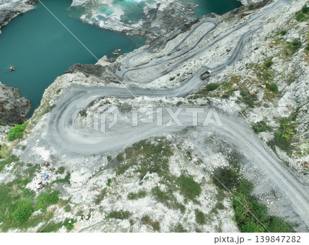 Aerial view of limestone quarry with heavy truck moving along winding road during mining operations, highlighting raw material supply, industrial activity, and environmental impact on landscape. 139847282