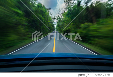 Front view of blue SUV car driving at high speed on asphalt road through green forest with motion blur effect, modern transportation and travel concept featuring dynamic movement. Adventure lifestyle. 139847426