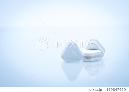 Triangle shape layered tablet pills for antacid digestive and gastric pain relief on white background in pharmaceutical concept. Multilayer formulation for effective treatment and healthcare use. 139847429