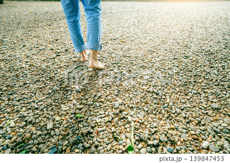 Close-up of barefoot woman walking on gravel ground in a peaceful forest retreat during early morning light. Self-care, emotional healing, and connection with nature for mental balance. Mindfulness. Close-up of barefoot woman walking on gravel ground in a peaceful forest retreat during early morning light. Self-care, emotional healing, and connection with nature for mental balance. Mindfulness. 139847453