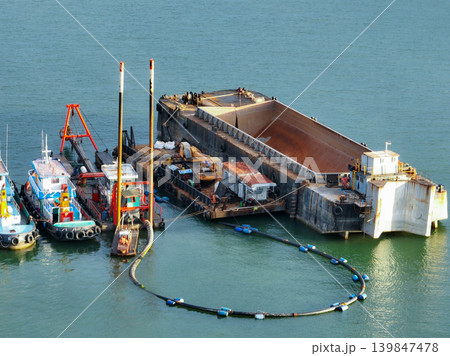 Heavy maritime engineering vessel conducting offshore dredging work with crane equipment and support boats in coastal waters for port deepening and marine construction infrastructure development Heavy maritime engineering vessel conducting offshore dredging work with crane equipment and support boats in coastal waters for port deepening and marine construction infrastructure development 139847478