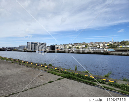 Peaceful River Scene with Plants and Buildings Under a Cloudy Sky Peaceful River Scene with Plants and Buildings Under a Cloudy Sky 139847556