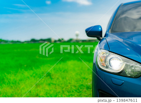 Front view of luxury blue compact SUV car with sport and modern design parked on green grass field with blue sky and white clouds. Hybrid auto and automotive. Road trip and car driving for travel. 139847611