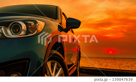 Blue compact SUV car with sporty modern design parked by the sea beach at sunset. Luxury crossover vehicle with dramatic red sky, travel lifestyle and premium automotive concept. Road trip adventure. 139847639