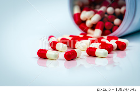 Red-white capsule pills on white table on blurred background of drug bottle. Antibiotics drug resistance. Antimicrobial capsule pills. Pharmaceutical industry. Pharmacy. Global healthcare concept. 139847645