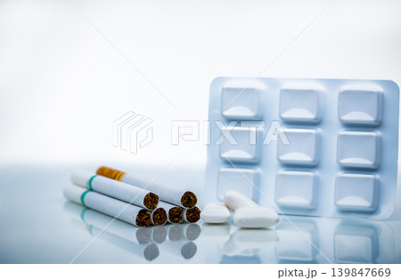 Nicotine chewing gum in blister pack near pile of cigarette. Quit smoking by use nicotine gum for relief of nicotine withdrawal symptoms. Medicine for giving up smoking. World no tobacco day concept. Nicotine chewing gum in blister pack near pile of cigarette. Quit smoking by use nicotine gum for relief of nicotine withdrawal symptoms. Medicine for giving up smoking. World no tobacco day concept. 139847669