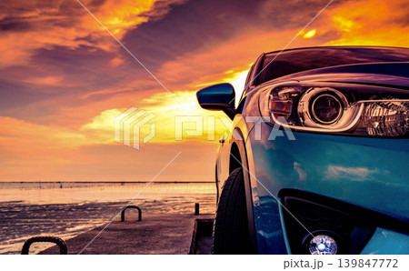 Blue SUV car parked on concrete pier by the sea during dramatic sunset, closeup headlight with golden sky. Travel road trip. Freedom, adventure and modern automotive lifestyle in coastal destination. Blue SUV car parked on concrete pier by the sea during dramatic sunset, closeup headlight with golden sky. Travel road trip. Freedom, adventure and modern automotive lifestyle in coastal destination. 139847772