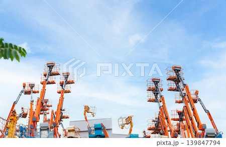 Articulated boom lift. Aerial platform lift. Telescopic boom lift against blue sky. Mobile crane parked at parking area for rent. Hydraulic boom lift at parking lot of crane dealership sale office. Articulated boom lift. Aerial platform lift. Telescopic boom lift against blue sky. Mobile crane parked at parking area for rent. Hydraulic boom lift at parking lot of crane dealership sale office. 139847794