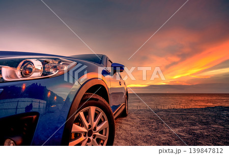 Blue compact SUV car with sport and modern design parked by beach at sunset. Hybrid and electric car technology. Car parking space. Automotive industry. Car care business background. Beautiful sky. 139847812