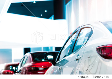 Rear view of white luxury car parked in modern showroom for sale. White shiny car on blurred red car in showroom. Car dealership. Coronavirus impact on automotive industry concept. Showroom interior. 139847850