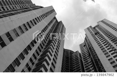 Bottom view of skyscraper building looking up against gray sky. Urban apartment, multi storey residential condo, corporate construction, and real estate development in city environment. Bottom view of skyscraper building looking up against gray sky. Urban apartment, multi storey residential condo, corporate construction, and real estate development in city environment. 139847902