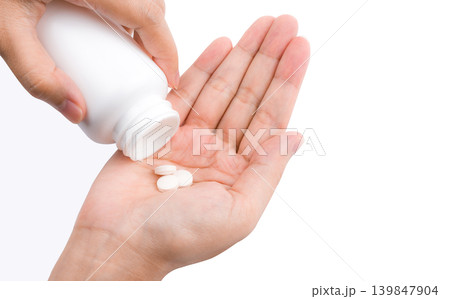 Woman hand pouring tablet pills from white plastic bottle into palm isolated on white background. Healthcare concept. Medication use, dosage control and daily treatment routine for adult patient care. Woman hand pouring tablet pills from white plastic bottle into palm isolated on white background. Healthcare concept. Medication use, dosage control and daily treatment routine for adult patient care. 139847904