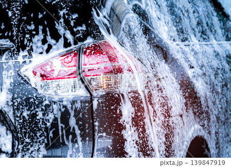 Rear view of black compact SUV car with sport and modern design are washing with water and white foam. Car care service business. Car covered with white foam. Car wash before and after travel concept. 139847919