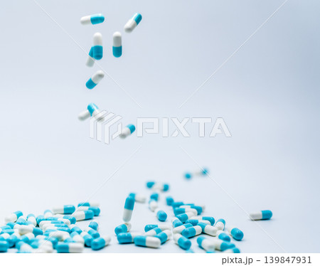 Blue-white capsule pill falling onto white table, antibiotic medication concept for responsible prescription use in healthcare. Antimicrobial resistance and patient safety in hospital or community. Blue-white capsule pill falling onto white table, antibiotic medication concept for responsible prescription use in healthcare. Antimicrobial resistance and patient safety in hospital or community. 139847931