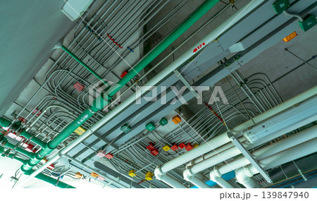 Electrical conduit system and galvanized steel pipe of electric cable installed on ceiling. PVC plastic pipe of drainage system and clean water on industrial building ceiling. Building construction. 139847940